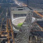 Gedung pencakar langit modern dengan stadion terbuka di puncaknya pada malam hari