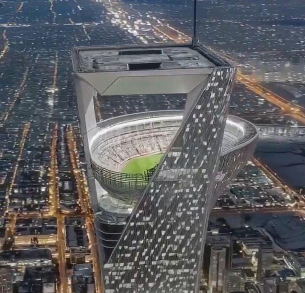 Gedung pencakar langit modern dengan stadion terbuka di puncaknya pada malam hari