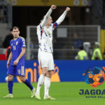 Pemain tim nasional melakukan selebrasi di lapangan setelah pertandingan, sementara pemain lawan berjalan di belakangnya dalam laga sepak bola internasional.