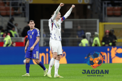 Pemain tim nasional melakukan selebrasi di lapangan setelah pertandingan, sementara pemain lawan berjalan di belakangnya dalam laga sepak bola internasional.