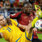 Dua pemain dari tim nasional berbeda berebut bola dalam duel sengit pada pertandingan sepak bola internasional, dengan logo Jagoan Super Bola di sudut kiri gambar.