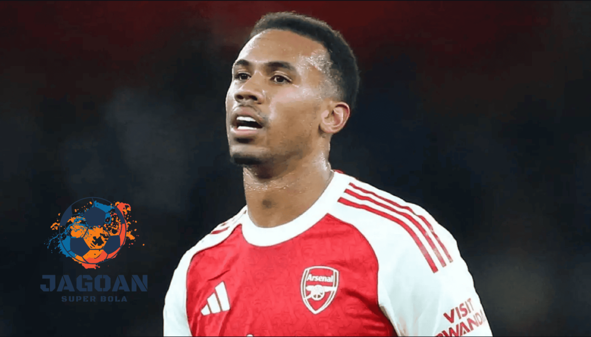 Seorang pemain Arsenal mengenakan jersey merah-putih sedang berada di lapangan saat pertandingan, dengan logo Jagoan Super Bola di bagian kiri gambar.