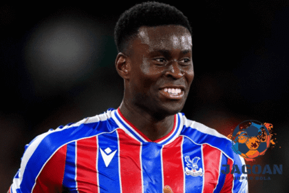 Seorang pemain Crystal Palace mengenakan jersey merah-biru sedang tersenyum di lapangan dalam pertandingan sepak bola.