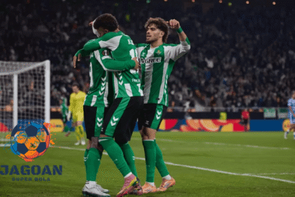 Pemain sepak bola Real Betis merayakan gol bersama di tengah pertandingan dengan logo Jagoan Super Bola pada sudut gambar.