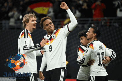 Para pemain tim nasional Jerman merayakan gol di lapangan dengan mengenakan jersey putih bergaris warna bendera Jerman.