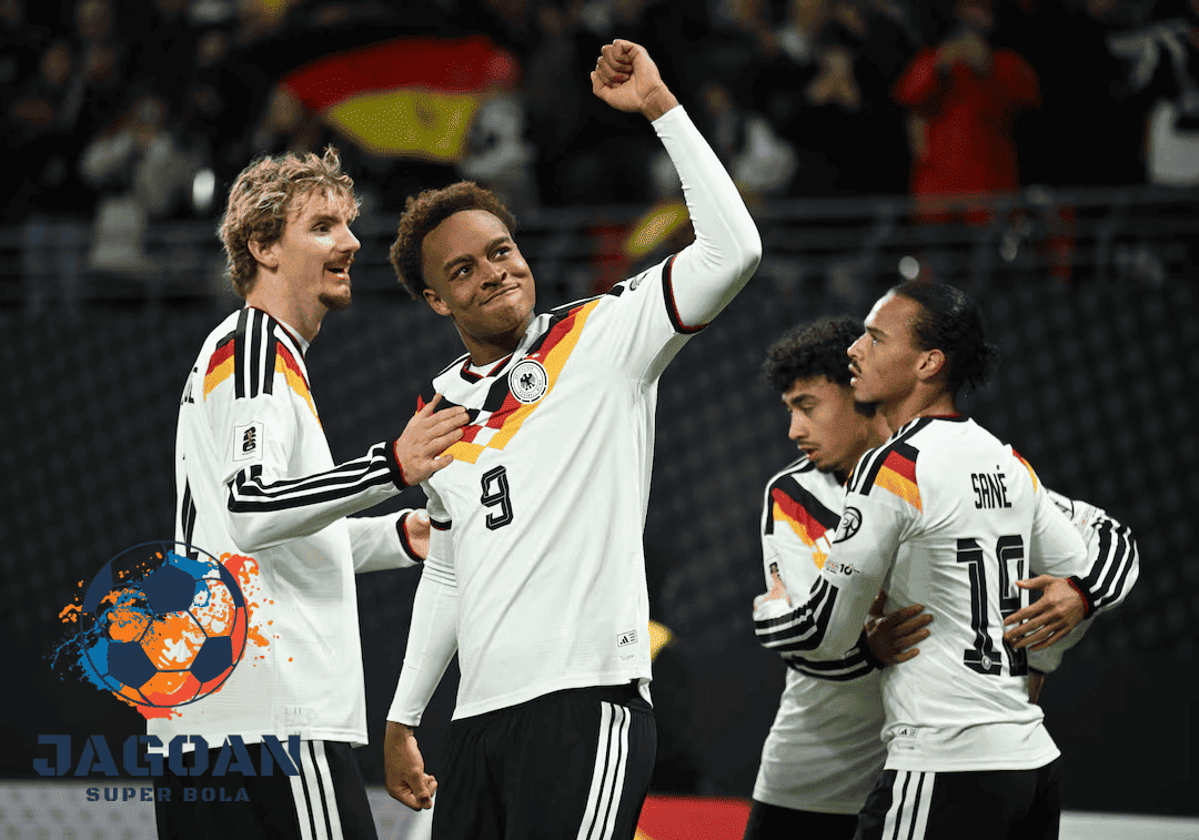 Para pemain tim nasional Jerman merayakan gol di lapangan dengan mengenakan jersey putih bergaris warna bendera Jerman.