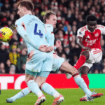 Pemain Arsenal menendang bola ke arah gawang melawan dua bek Brentford dalam pertandingan sepak bola, dengan logo Jagoan Super Bola di sudut kiri gambar.