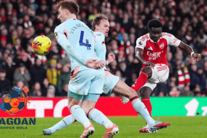 Pemain Arsenal menendang bola ke arah gawang melawan dua bek Brentford dalam pertandingan sepak bola, dengan logo Jagoan Super Bola di sudut kiri gambar.