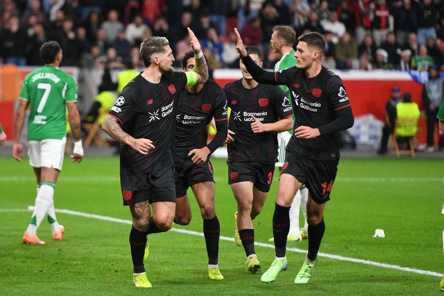 Pemain Bayer Leverkusen mengenakan jersey hitam dengan sponsor Barmenia merayakan gol di pertandingan sepak bola kandang dengan latar penonton penuh.