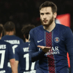 Seorang pemain PSG melakukan selebrasi di lapangan dengan rekan setim di latar belakang.