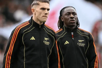 Eberechi Eze dan Viktor Gyökeres mengenakan jersey training hitam bergaris oranye Adidas dengan sponsor Emirates, berhadapan di dalam stadion selama sesi pemanasan atau pertandingan.