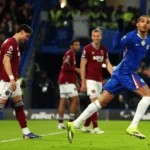 Pemain Chelsea merayakan gol dengan lari penuh semangat di Stamford Bridge, sementara pemain West Ham dengan jersey merah anggur terlihat kecewa di belakangnya saat Chelsea menang 3-2.