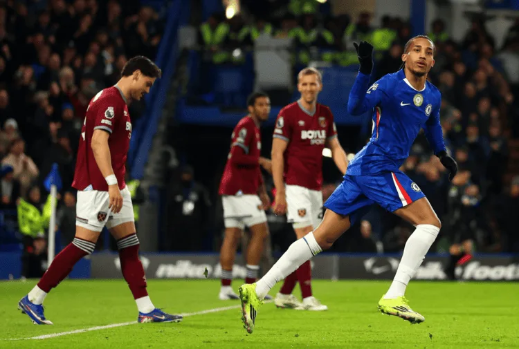 Pemain Chelsea merayakan gol dengan lari penuh semangat di Stamford Bridge, sementara pemain West Ham dengan jersey merah anggur terlihat kecewa di belakangnya saat Chelsea menang 3-2.