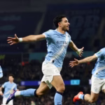 Pemain Manchester City dengan seragam biru langit merayakan kemenangan skor 3-1 melawan Newcastle United dengan mengangkat tangan di tengah lapangan.