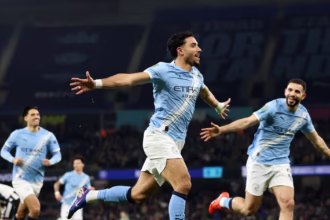Pemain Manchester City dengan seragam biru langit merayakan kemenangan skor 3-1 melawan Newcastle United dengan mengangkat tangan di tengah lapangan.