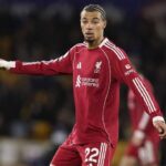 Hugo Ekitike Liverpool FC nomor 22 mengenakan jersey merah Adidas panjang lengan sponsor Standar Chartered, berpose dengan jari telunjuk di lapangan sepak bola - Bola188