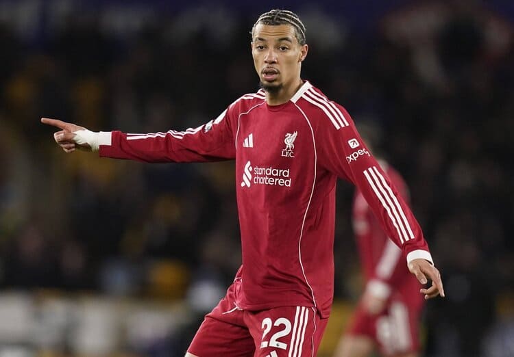 Hugo Ekitike Liverpool FC nomor 22 mengenakan jersey merah Adidas panjang lengan sponsor Standar Chartered, berpose dengan jari telunjuk di lapangan sepak bola - Bola188